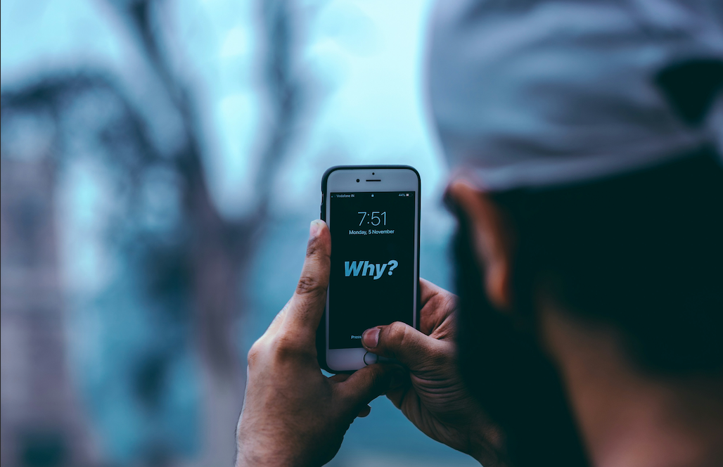 An image of a man holding a phone with 'Why?' written on it.